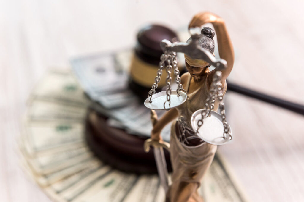 A Lady Justice statue holding scales stands in front of a judge's gavel and fanned money, symbolizing the legal consideration of financial assets and spousal support in high-net-worth divorce cases.